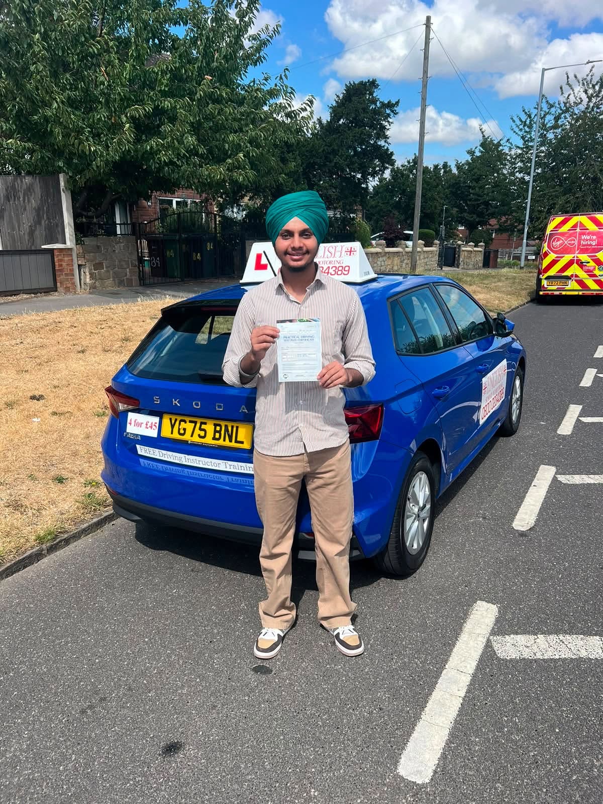 Newly qualified driver holding a practical test pass certificate beside a branded English School of Motoring car